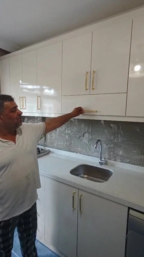 Müşterimizin yanında beyaz mutfak dolapları, metal kulplar ve evye çevresini gösteren gerçek video karesi