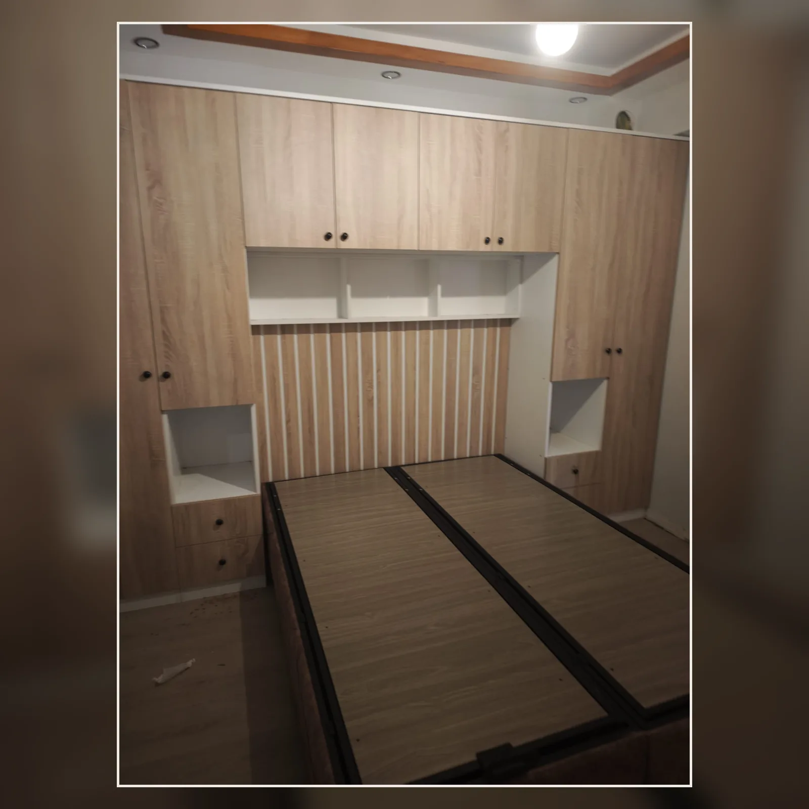 Çift bazalı yatak önünde üst dolap, raf ve yan depolama modülleri bulunan yatak odası